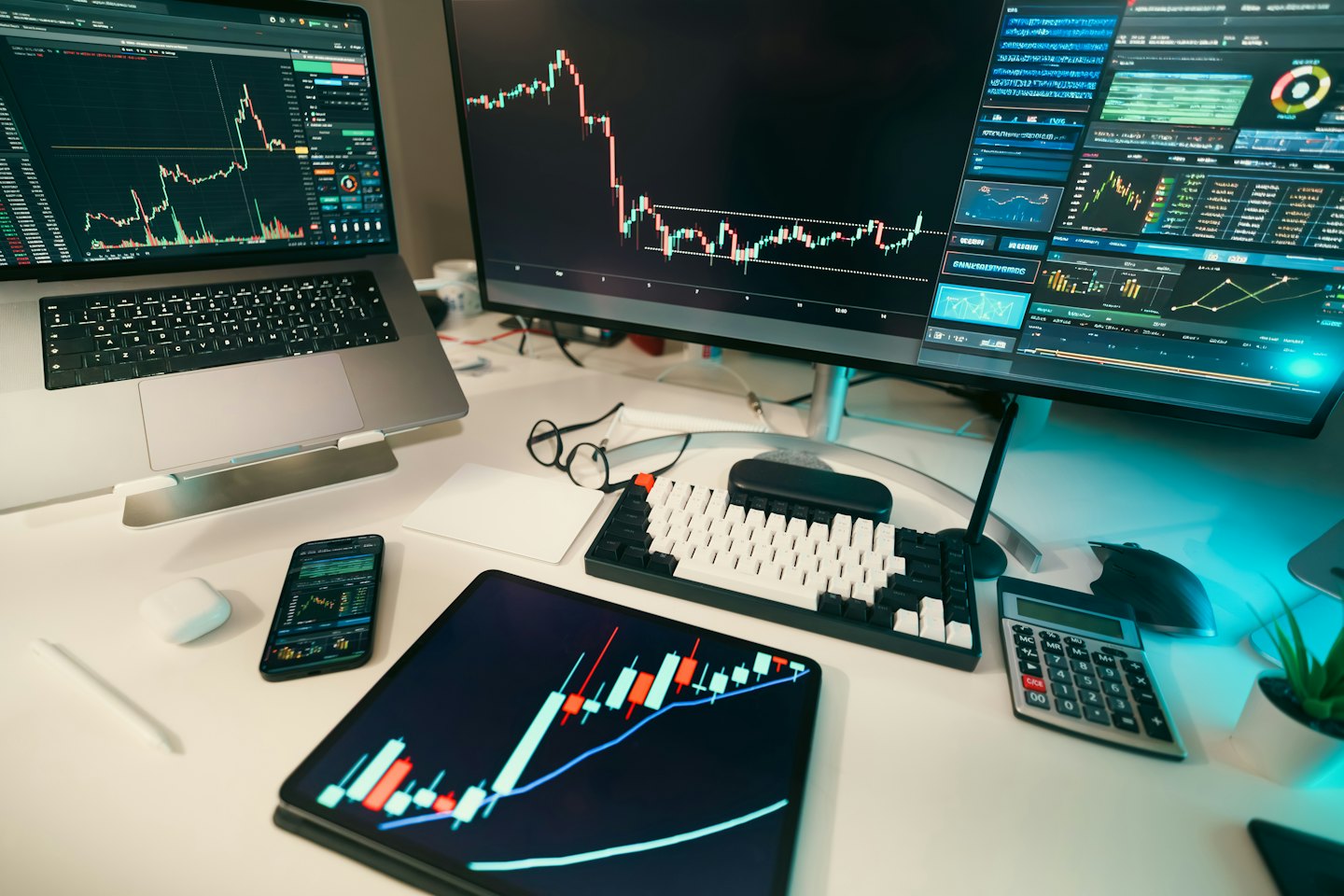 Laptop, monitor, tablet, and phone display stock market data.